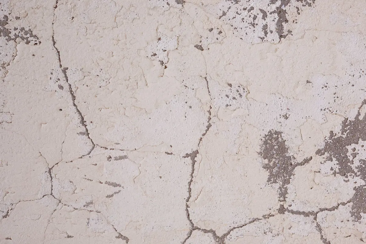 Fissures de retrait et écaillage visibles à la surface d'une dalle de béton mal curée.