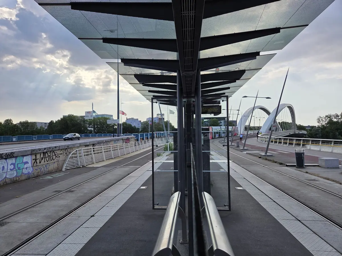 Tramway moderne à l'arrêt près d'une gare avec voyageurs attendant
