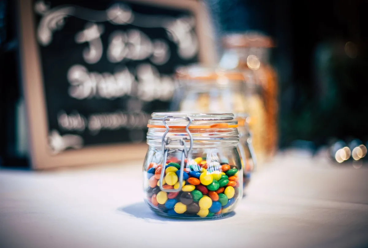 Bocal transparent rempli de bonbons colorés : gommes fruitées, chocolats et caramels portionnés